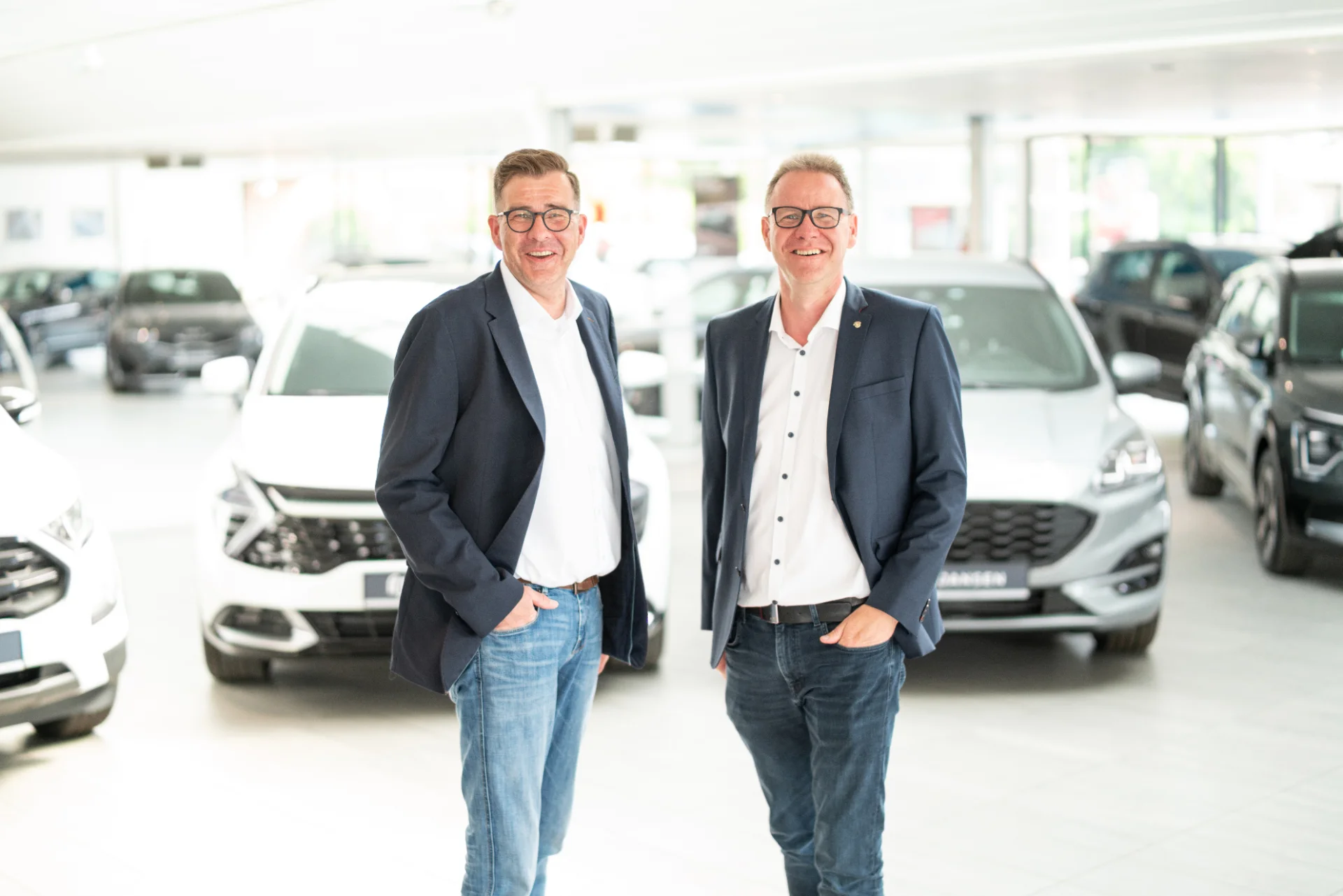 Zwei Inhaber des Autohaus Jansen im hellen Showroom mit mehreren Fahrzeugen